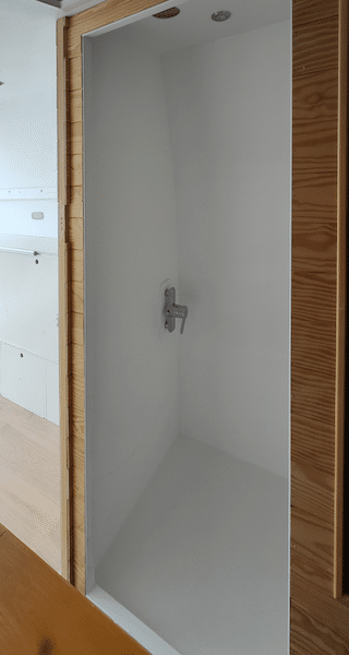 Mini douche d’intérieur de fourgon aménagé avec robinet et receveur blanc, parois lisses et accès dégagé.