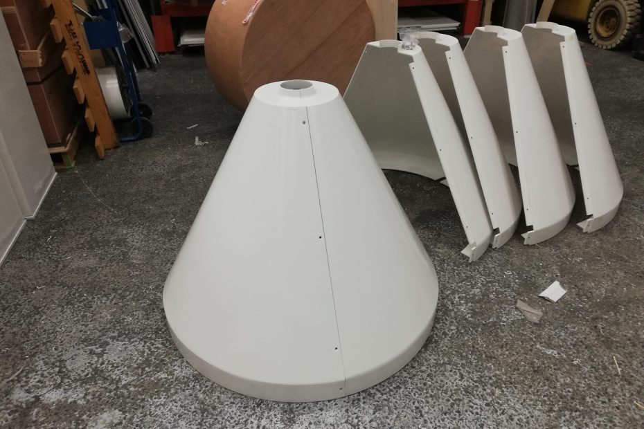 Pyramide en métal blanc et cônes décoratifs, pièces rangées sur le sol dans un atelier, contexte de fabrication de plexiglass sur mesure pas cher.
