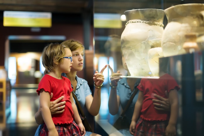 Vitrine musée en plexiglas exposant un objet historique dans une salle lumineuse; deux enfants observent à travers la vitre, mettant en avant la transparence et la clarté du plexiglas
