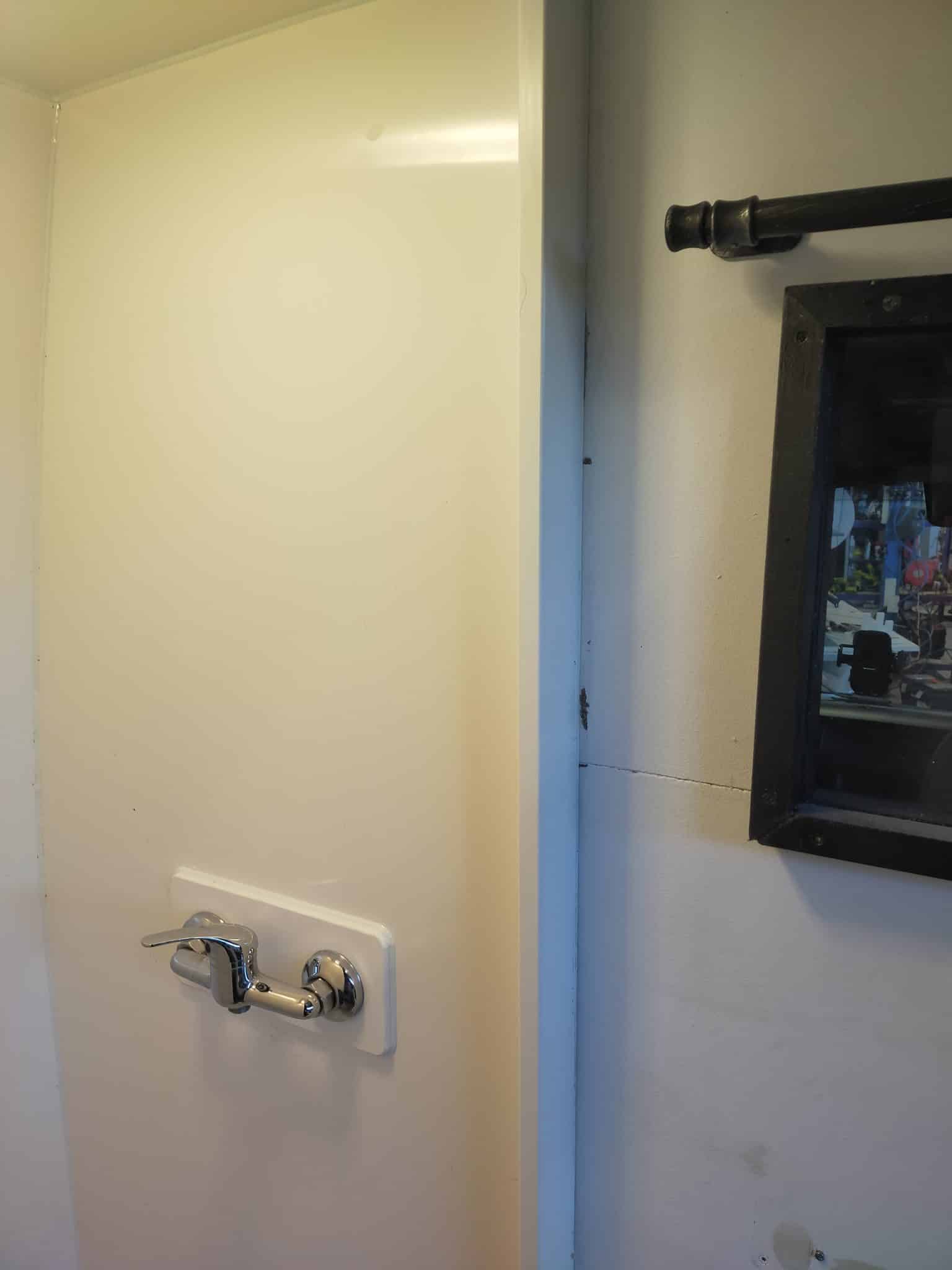 Douche simple dans un van aménagé: paroi blanche, robinet et pommeau symétriques, espace compact pour la fabrication douche van aménagé.